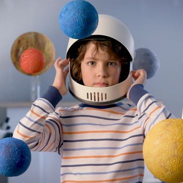 Child wearing astronaut helmet surrounded by colorful planets.