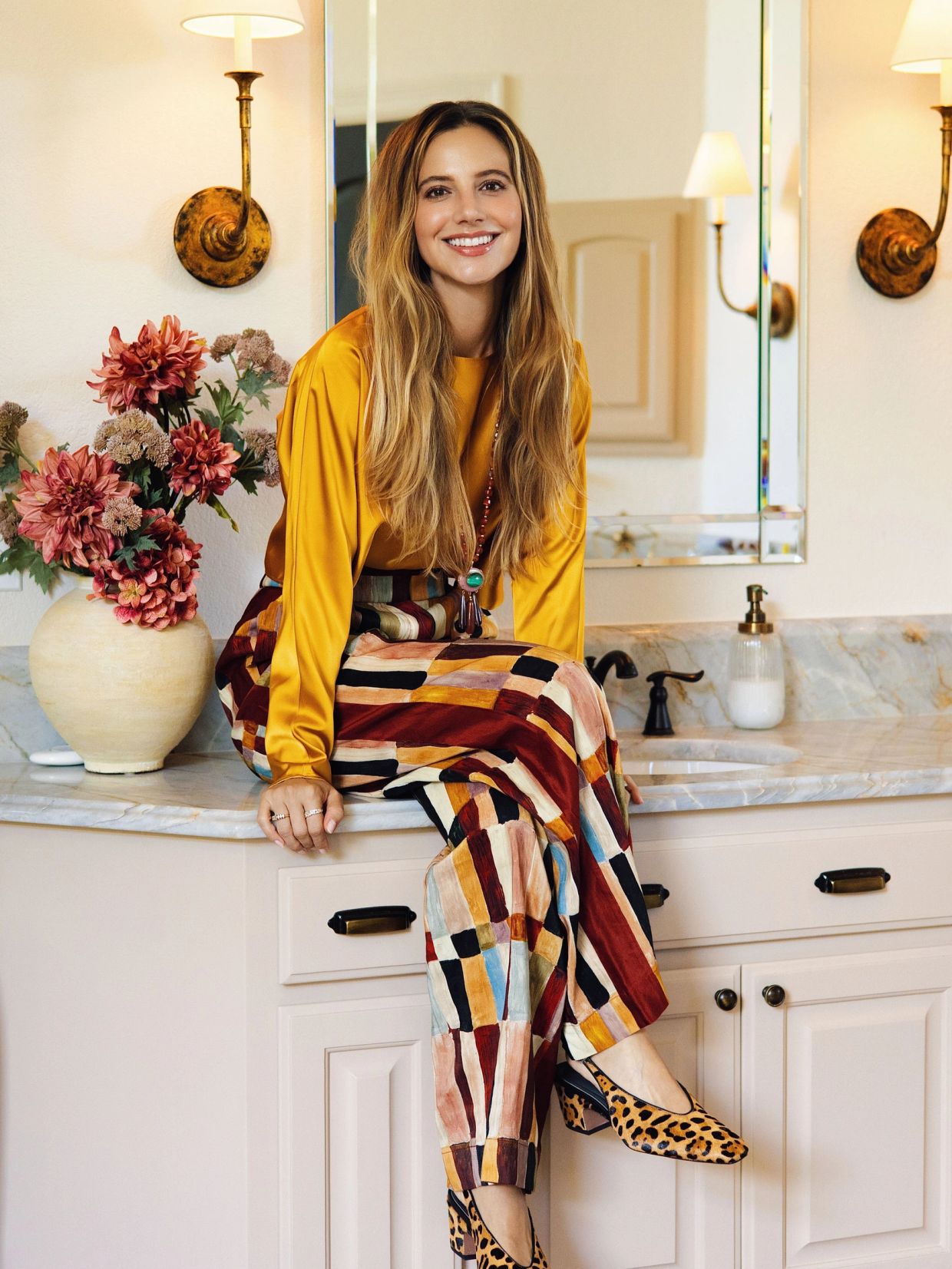 Woman smiling while sitting on a bathroom counter.