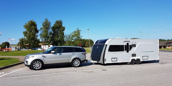 Silver SUV towing a modern white caravan in a parking lot on a clear day.