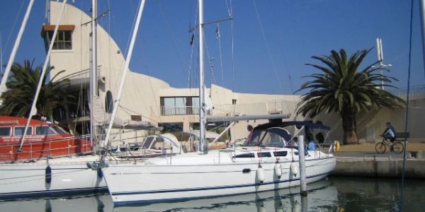 White sailboat docked near a building with palm trees under a clear blue sky.