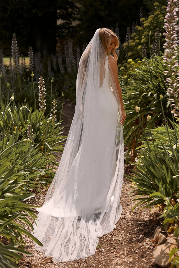 Bride in flowing gown and veil in a sunlit garden