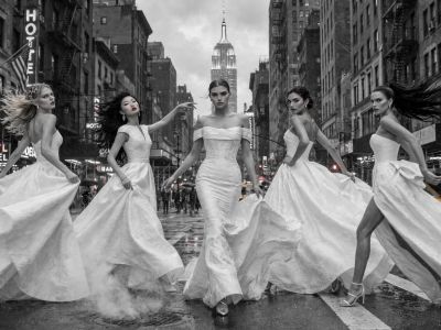 Five women in elegant dresses posing on a city street.