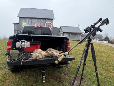Hunting gear and game on a pickup truck with a sniping rifle on a tripod.