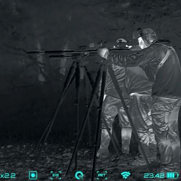 Thermal camera view of hunters behind a precision tripod setup during a guided nighttime predator hu