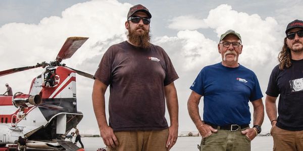 Three men standing near a helicopter.