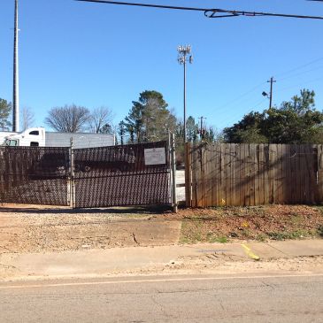 A closed metal gate next to a wooden fence under a clear sky.