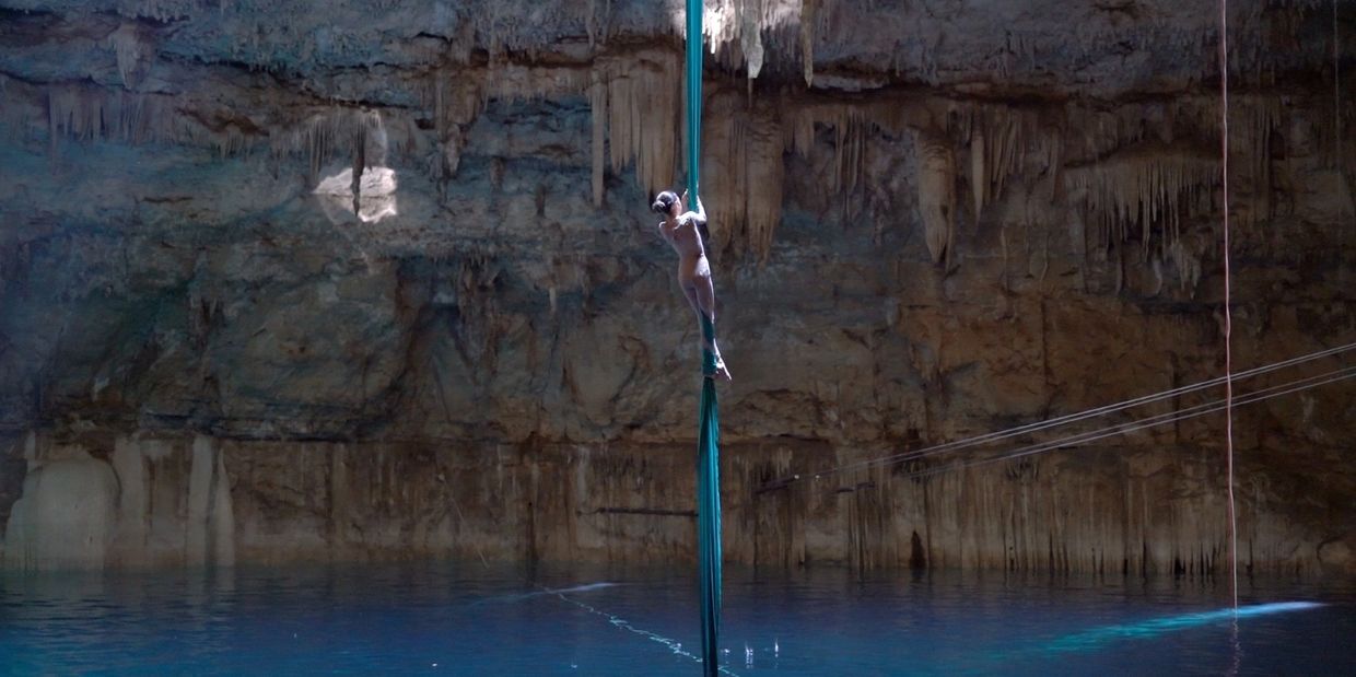Aerial silk artist performing inside a cave over water.
