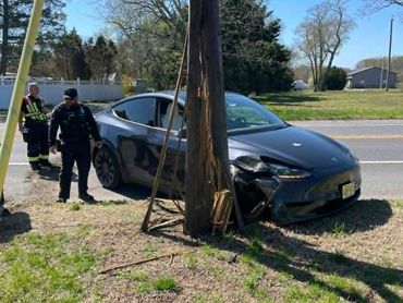 Black car crashed into a wooden utility pole with police nearby.