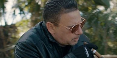 Man in leather jacket smoking a cigar outdoors.