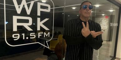 Man posing inside a radio station with WP RK 91.5 FM logo on glass.