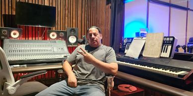 Man in recording studio producing a song, surrounded by audio equipment.