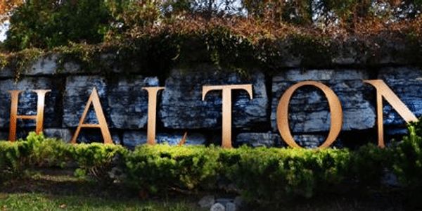 Large metal letters spelling 'HALTON' on a stone wall with greenery.