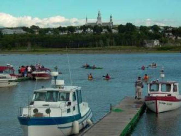 Boats and kayaks on a calm river near a dock with a distant church skyline.