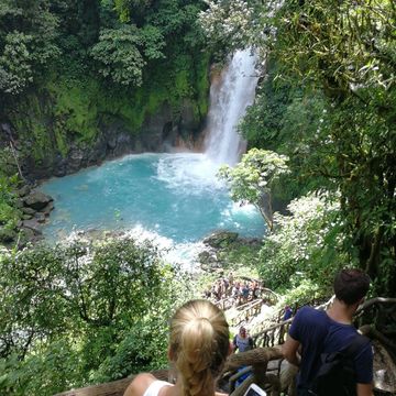 La imagen muestra a personas bajando a Rio Celeste. vemos una hermosa catarata 