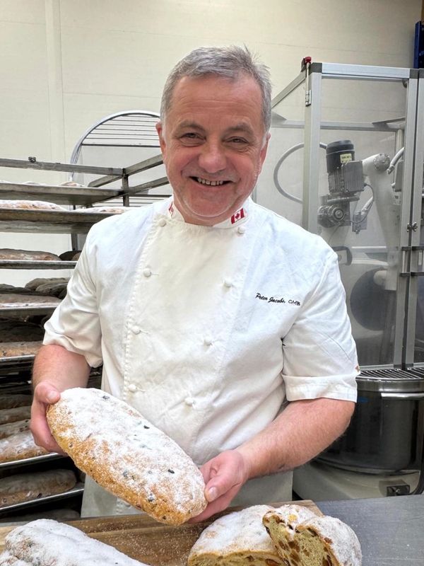 Smiling baker holding freshly baked, powdered bread in a bakery kitchen.