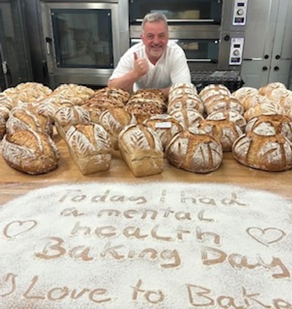 Man smiles behind a table full of freshly baked bread with a message in flour.