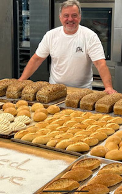 Smiling baker showcases an array of freshly baked breads and rolls.