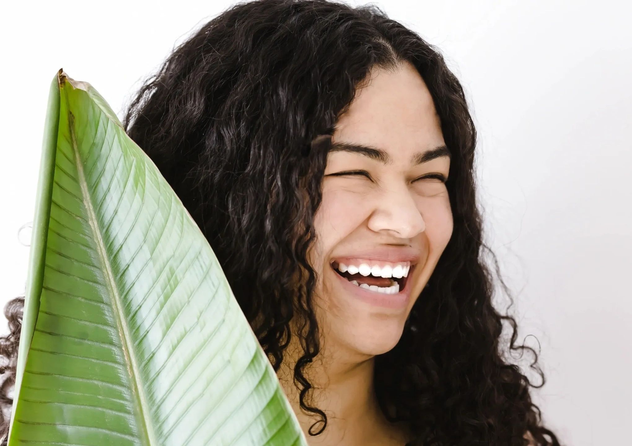 Laughing young woman holding a shiny tropical leaf.