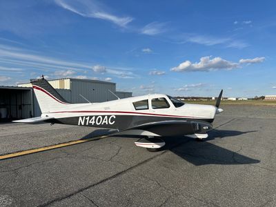 Small single-engine airplane parked on tarmac under blue sky.