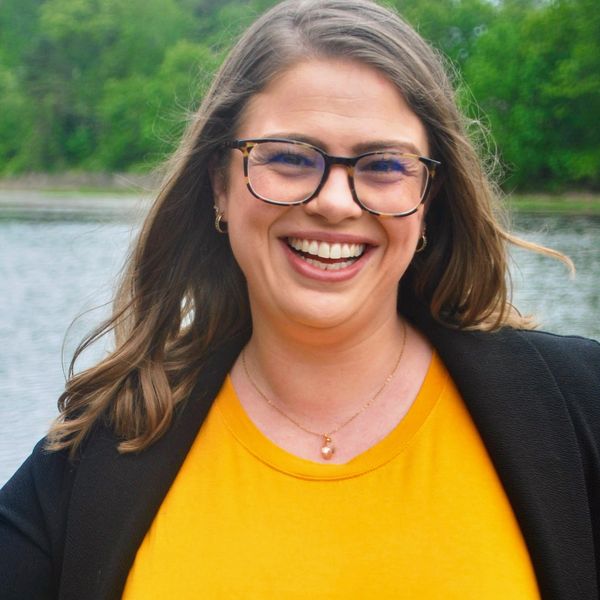 Smiling woman in yellow dress outdoors near water.