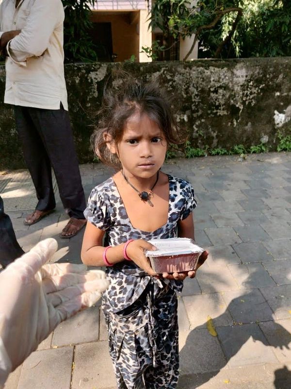 A small girl standing road side holding a food packet in her hand 