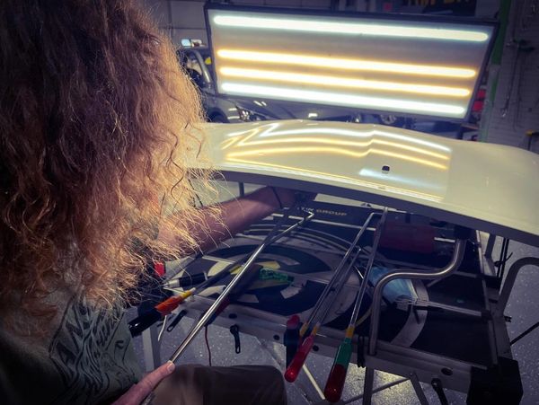 Person repairing a car door with specialized tools under a bright light.
