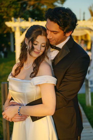 Couple embraces tenderly outdoors at sunset, dressed in elegant formal attire.