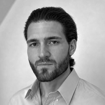 Black and white portrait of a serious man with a beard and slicked-back hair.