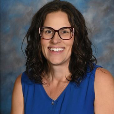 Smiling woman with curly hair and glasses in blue top.