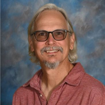 Smiling man with glasses and a red shirt.