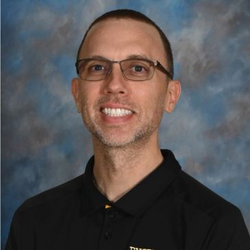 Smiling man with glasses in black polo shirt.