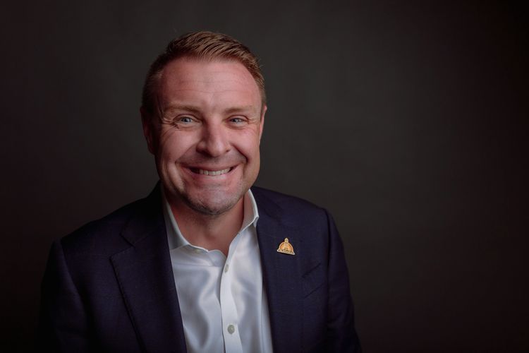 Smiling man in a suit jacket against a dark background.