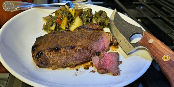Grilled steak with vegetables on a white plate and a wooden-handled knife.