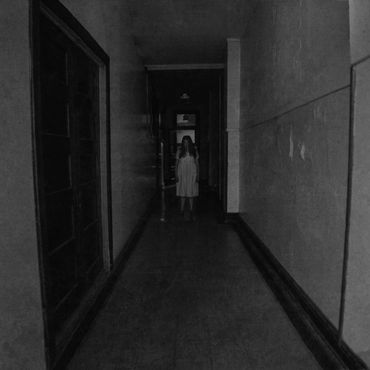 Creepy woman standing at the end of a spooky hallway.