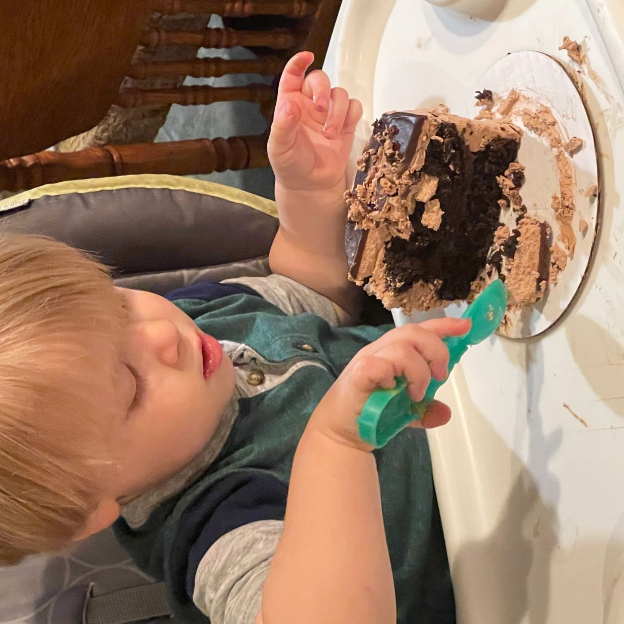 A toddler eagerly eating a piece of chocolate cake with a spoon.