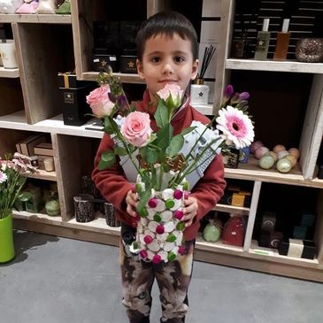 A young boy holding a colorful flower bouquet in a decorated vase.