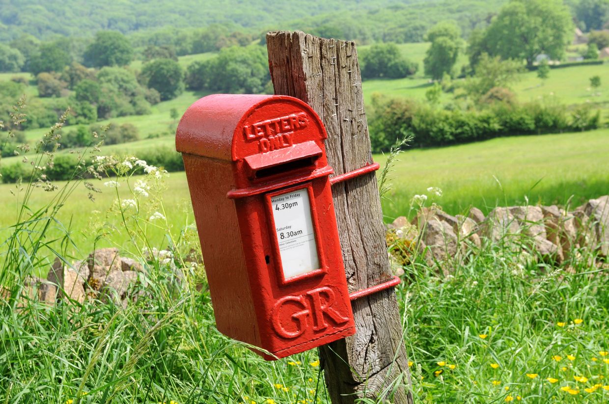 Red mailbox attached to a wooden post in a green rural field.