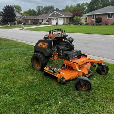 Orange SCAG lawn mower on green grass near suburban street.