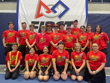 A team in matching red shirts posing in front of a banner.