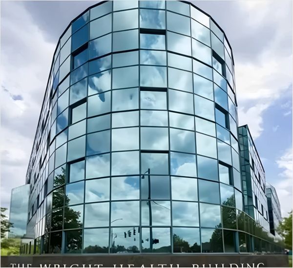 Modern glass building reflecting clouds, titled "The Wright Health Building,"
