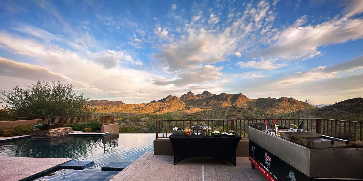 Tacos Trafi Catering setup by an infinity pool with scenic desert mountain under a vibrant sky.