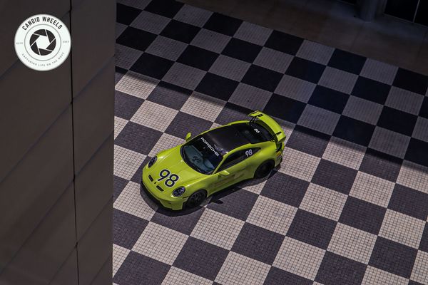 Green Porsche with racing number 98 parked on checkered tiles.