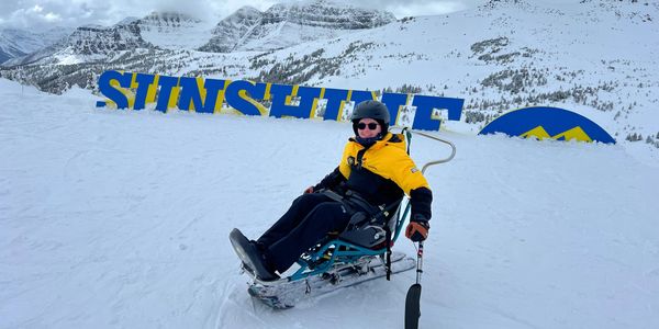 Mac in a sit ski on ski hill in front of Sunshine mountain sign