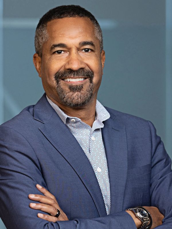 Smiling man wearing a blue suit jacket and patterned shirt.