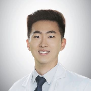 Young man in a white coat and tie smiling at the camera.