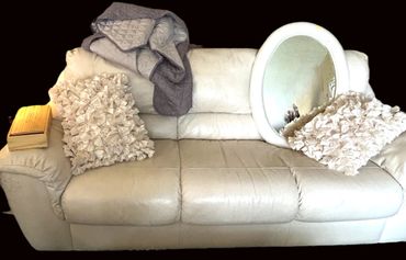 White leather sofa with textured pillows and a round mirror.