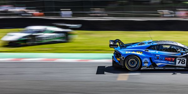 Blue race car speeding on a track with a blurred competitor in the background.