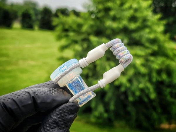 Hand holding a small glass pipe with a colorful wrapped coil against a green outdoor background.