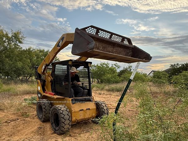 A cowboy working a skid steer on The Tilton Farm, attempting to install steel T Posts for a fence.