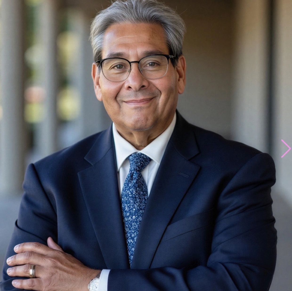 Confident man in a suit with glasses smiling warmly at the camera.